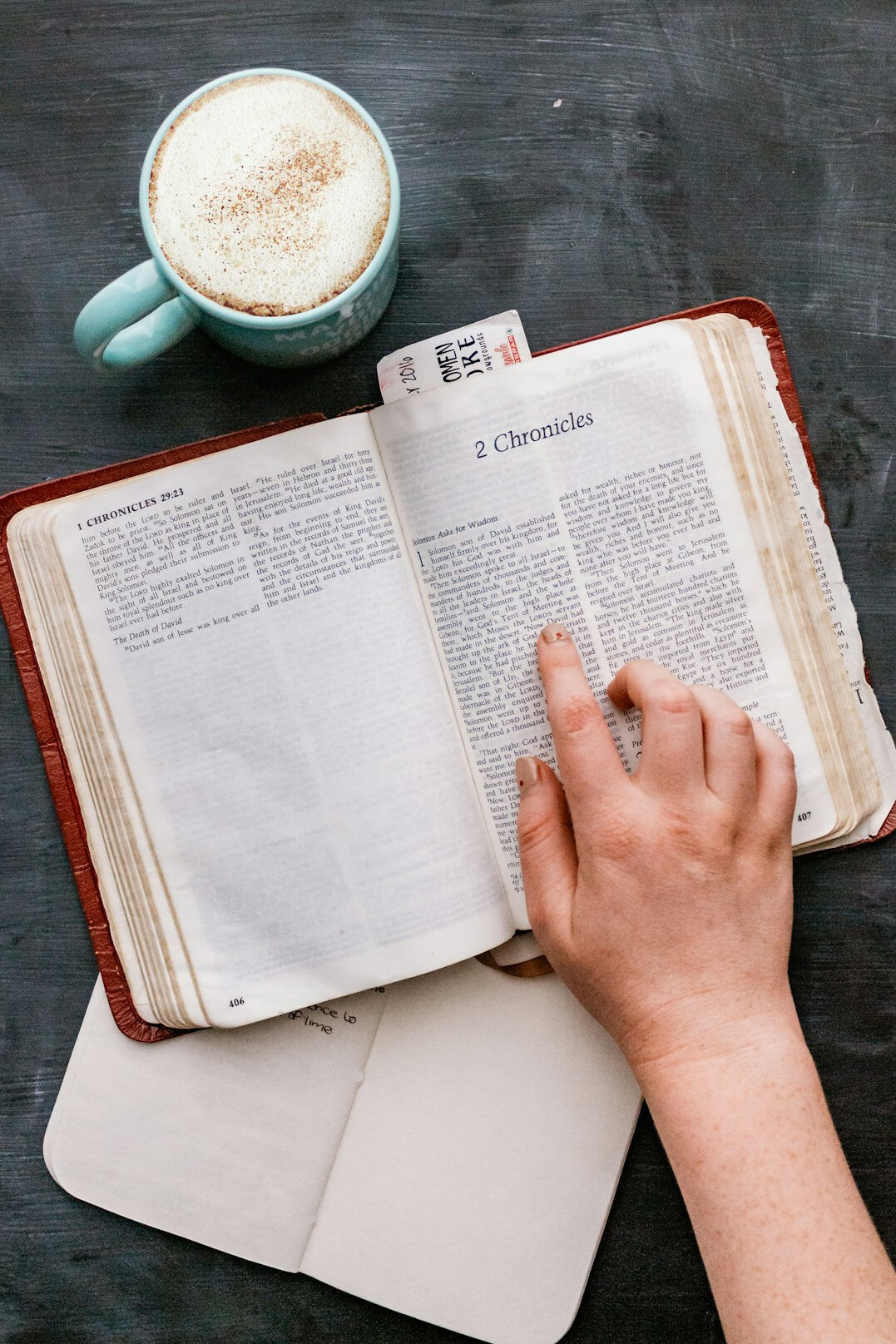 Hand writing a list in a notebook next to a mug